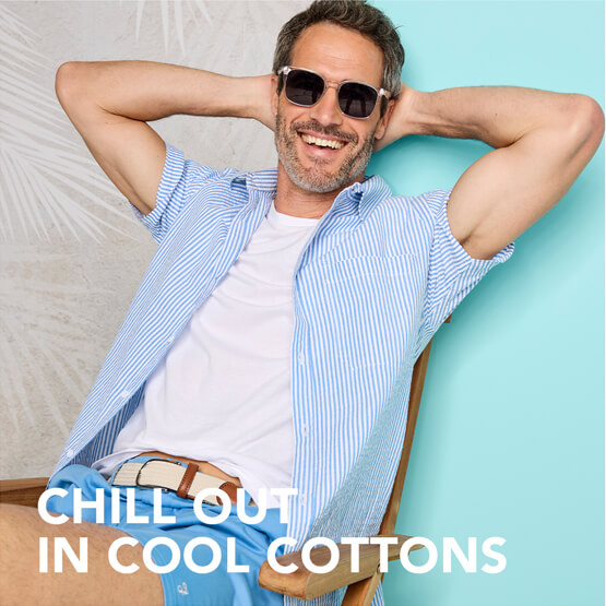 A male model, looking laid back in his chair, smiling, wearing sunglasses and a cool cotton shirt and top.collection of blankets, rugs and runners styled over a stand.